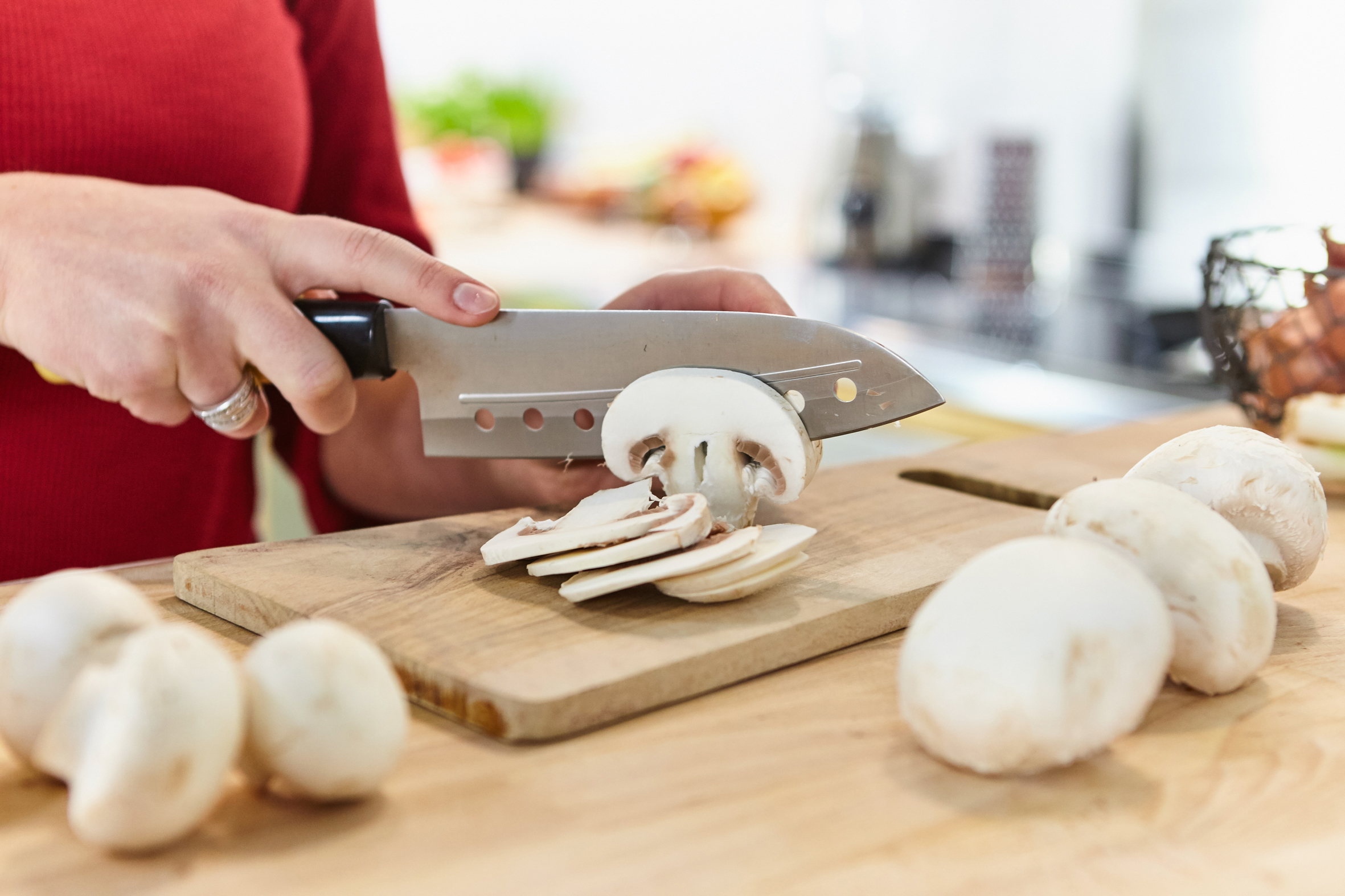 Frau schneidet weiße Champignons mit Messer auf Holzbrett