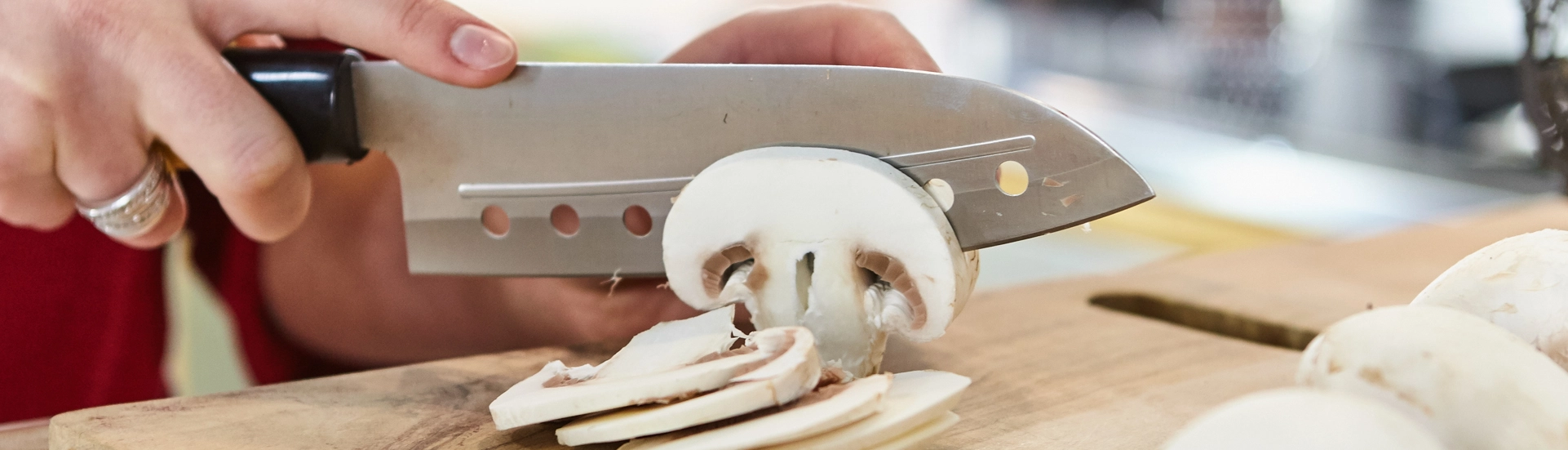 Frau schneidet weiße Champignons mit einem Messer auf einem Holzbrett