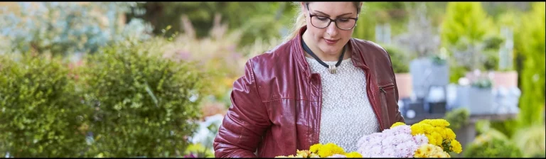Frau schaut auf blühende Pflanzen, die sie in einem Gartencenter in der Hand hält