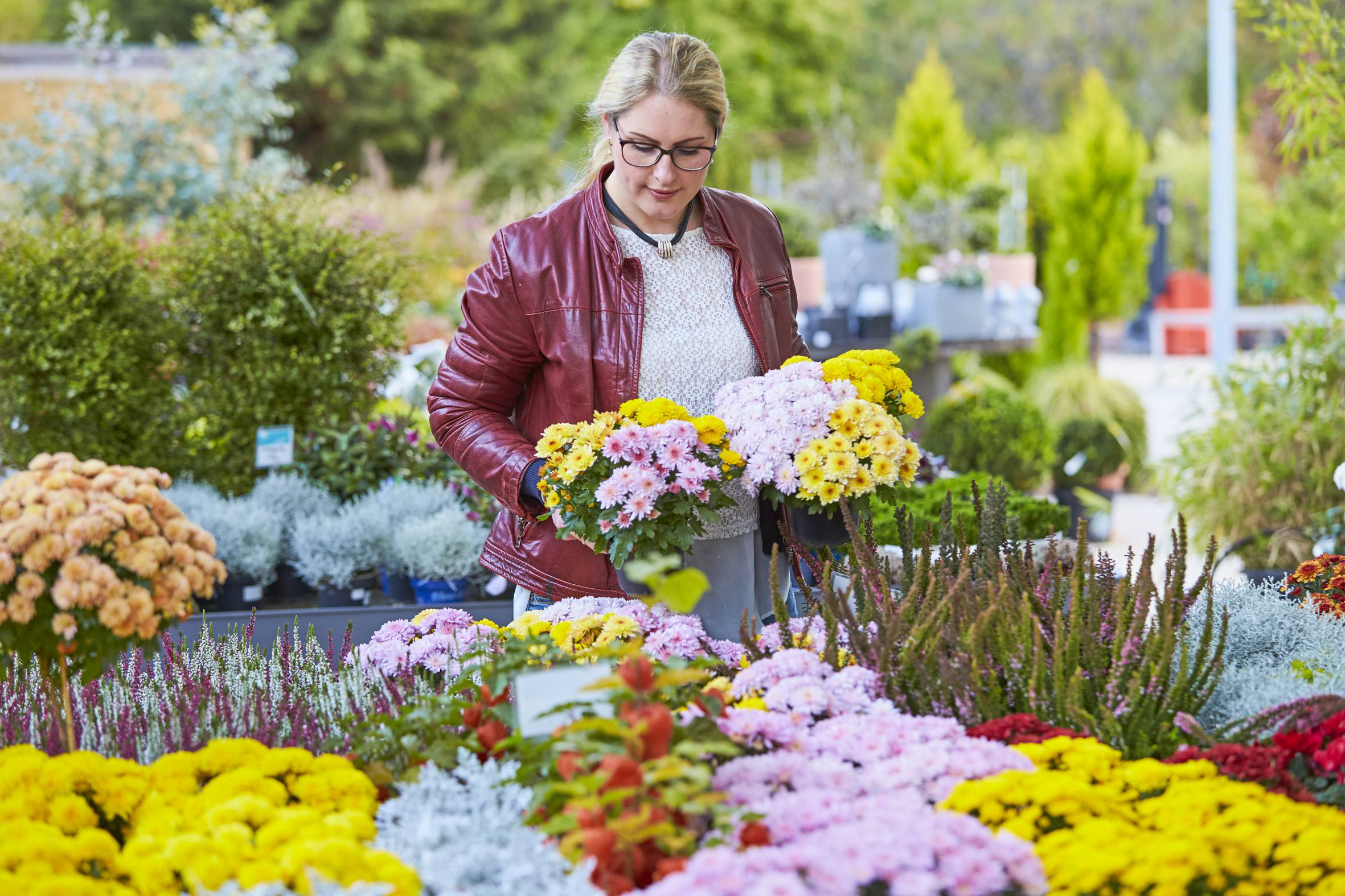Frau schaut auf blühende Pflanzen, die sie in einem Gartencenter in der Hand hält.